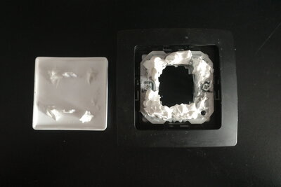 Damit die Abdeckung wieder hält, aber noch abnehmbar bleibt, habe ich die auf das kleine Metallblech geklebt. Das Blech selbst wird von seinen Federn fest genug im festgeschraubten Metallstück gehalten. Ich habe einfaches Silikon genommen, weil es gerade da lag. Ein ähnlich viskoser Kleber funktioniert natürlich auch. Es braucht schon eine Dicke Schicht davon, weshalb flüssige Kleber meiner Ansicht nach nicht geeignet sind. Auch nicht mit Heißkleber zum Fixieren. Der Kleber sollte ein bisschen Abstand zum Rahmen haben, damit dieser nicht auch angeklebt wird. Einfach ein bischen etwas auftragen, Abdeckung aufsetzen, sehen wie viel davon an der Abdeckung an kam und ggf. mehr Kleber auftragen. Aufhören bevor so viel Kleber beim Aufsetzen der Abdeckung zur Seite gedrückt wird, dass der Rahmen welchen abbekommt.